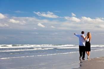 A young man and woman couple having a romantic walk on a beach with a bright blue sky