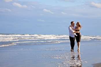 A young man and woman couple having romantic fun walking and embracing on a beach with a bright blue sky