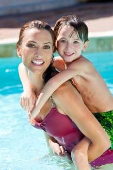 A beautiful mother having fun with her son on her shoulders in a swimming pool