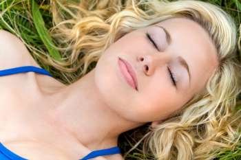 A beautiful young woman asleep in a grassy field with a smile on her face