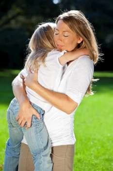 A young mother with her blond daughter cuddling and having fun in a sun bathed green park
