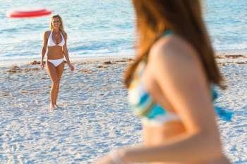 A beautiful young blond woman wearing a white bikini playing frisbee at the beach with her friend