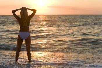 A beautiful bikini clad blond stands in the surf at sunset