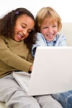 Two young children surfing the wold wide web on a laptop while sitting on a settee