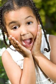 A beautiful mixed race little girl hands up to her face and expressing happy surprise. The shot is taken in natural summer sunshine.