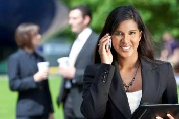 A beautiful young Asian businesswoman with a wonderful smile shot using her cell phone outside with her colleagues out of focus behind her.