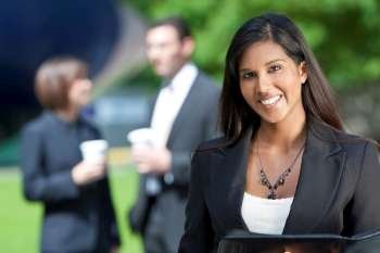 A beautiful young Asian businesswoman with a wonderful smile shot outside with her colleagues out of focus behind her.