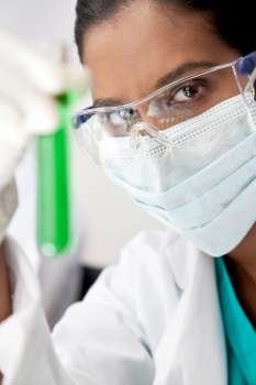 A female Asian medical or scientific researcher or doctor looking at a test tube of a green solution in a laboratory.