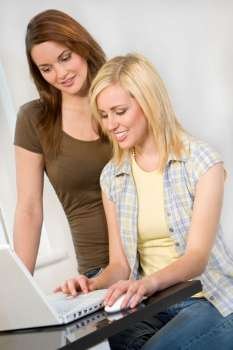 Two beautiful young women at home in the kitchen using a laptop computer to surf the web.