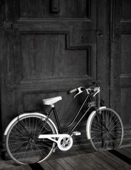 Aged vintage black bicycle, big wooden door, black and white