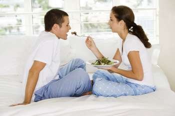 Side profile of a young woman feeding a young man salad