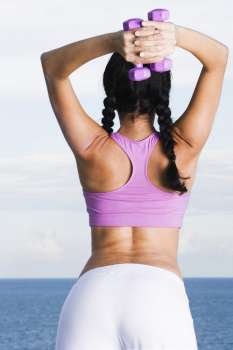 Rear view of a young woman exercising with dumbbells