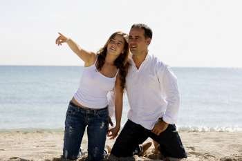 Young woman pointing forward to a mid adult man on the beach