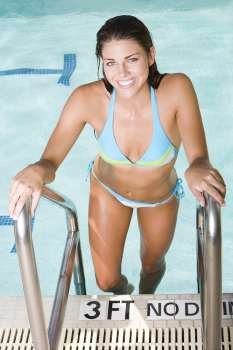 Portrait of a young woman climbing up a swimming pool ladder