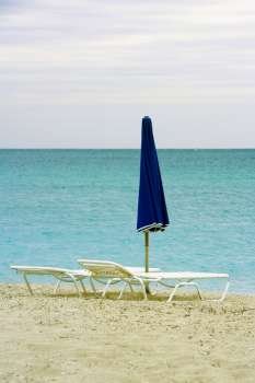 Empty lounge chair and a folded beach umbrella on the beach