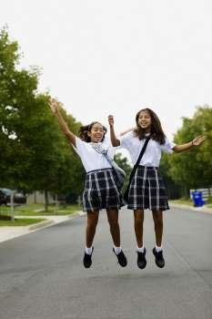 Two schoolgirls jumping on the road