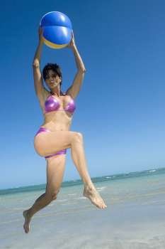 Low angle view of a mid adult woman playing with a beach ball on the beach