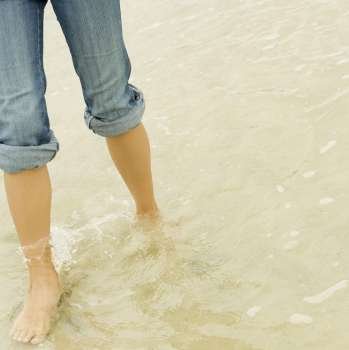 Low section view of a young woman wading in water on the beach
