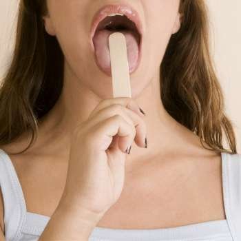 Close-up of a young woman using a tongue depressor to examine her tongue