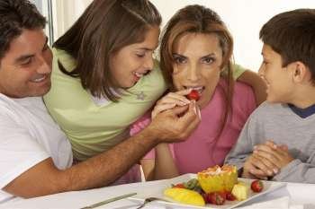 Mid adult man feeding a mid adult woman a strawberry with their two children beside them