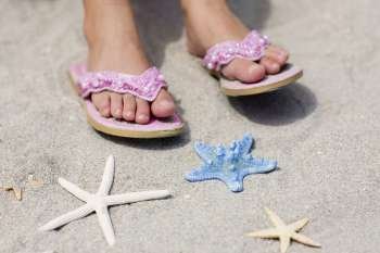 Close-up of a person´s feet on the beach near three starfish