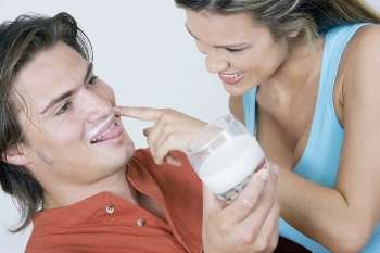 Close-up of a young woman touching milk mustache of a young man and smiling