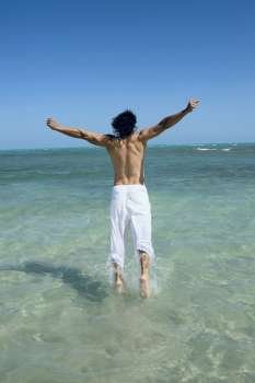 Rear view of a mid adult man jumping on the beach with his arms outstretched