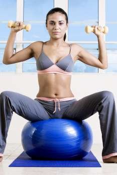 Portrait of a young woman exercising with dumbbells on a fitness ball