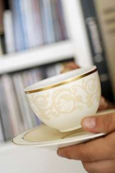 Close-up of a person´s hand holding a cup of tea and a saucer