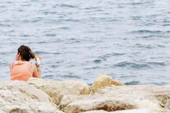 Rear view of a woman sitting at the seaside, Baie De Cannes, Cote d´Azur, Cannes, Provence-Alpes-Cote D´Azur, France