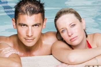 Portrait of a young man and a young woman leaning at the edge of a swimming pool