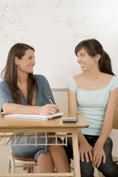 Teenage girl sitting in a classroom with her female teacher and smiling