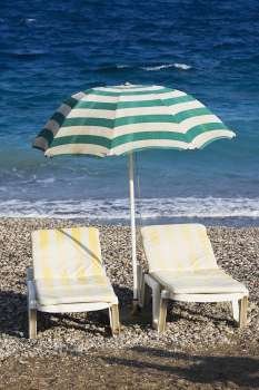 Two lounge chairs under a beach umbrella on the beach, Greece