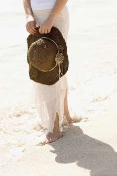 Low section view of a young woman holding a sunhat on the beach