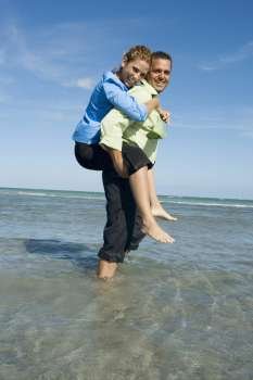 Side profile of a mid adult woman riding piggyback on a mid adult man on the beach
