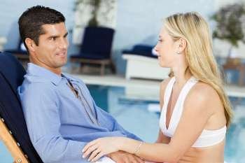 Young woman and a mid adult man sitting at the poolside