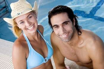Portrait of a young woman and a mid adult man smiling at the poolside