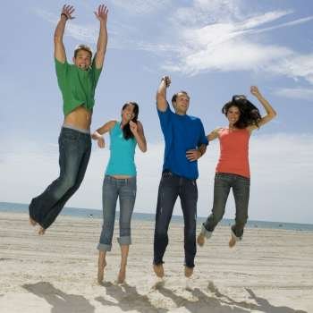 Low angle view of two young couples jumping on the beach and smiling