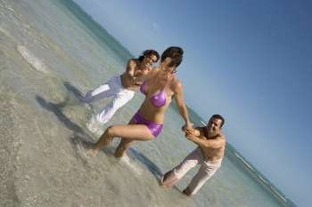 Mid adult woman pulling two mid adult men on the beach