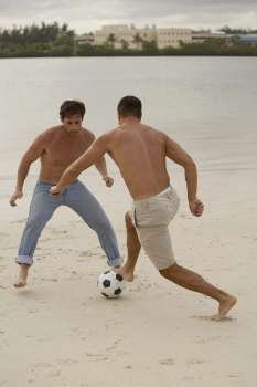 Rear view of a mid adult man playing soccer with a young man on the beach
