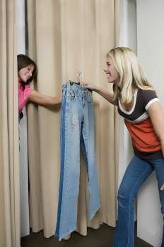 Young woman taking jeans from a sales clerk in a fitting room