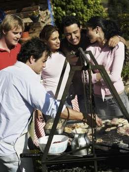 Mid adult man preparing food in a barbecue grill with four people standing beside him