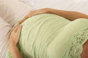 Mid section view of a pregnant woman lying on the bed touching her abdomen