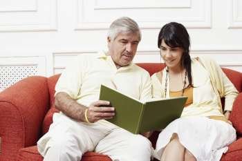 Mature man sitting with his daughter on a couch and reading a book