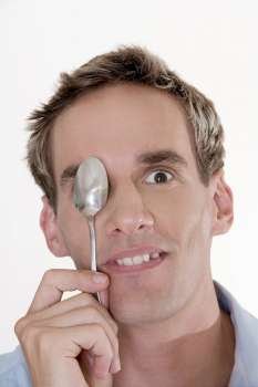 Portrait of a mid adult man holding a spoon in front of his eye