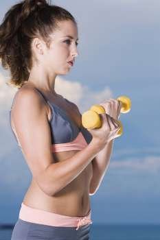 Side profile of a young woman exercising with dumbbells