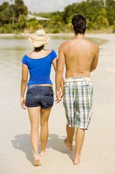 Rear view of a young man and a teenage girl walking on the beach