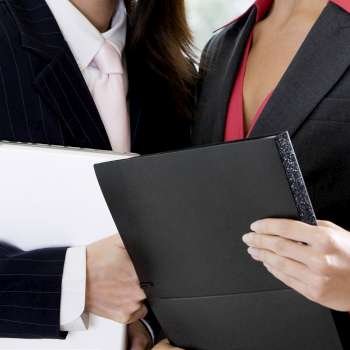 Mid section view of two businesswomen holding a file and a laptop