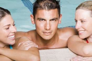 Portrait of a young man and two young women leaning at the edge of a swimming pool