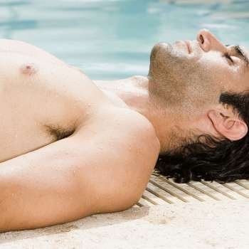 Side profile of a mid adult man lying at the edge of a swimming pool